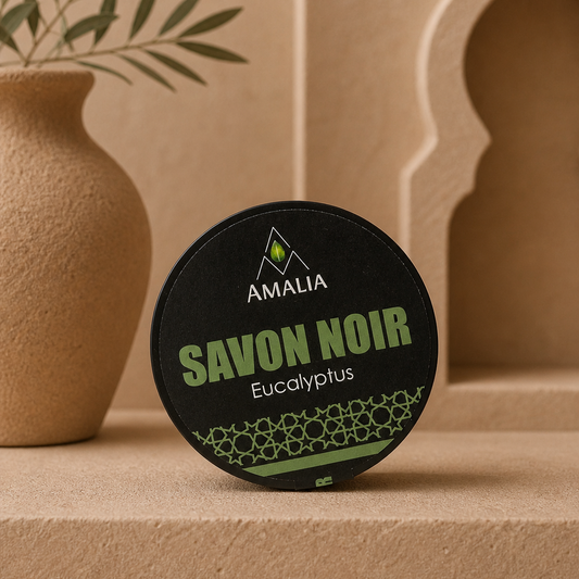 Amalia Savon Noir Eucalyptus soap bar on a beige surface with a decorative vase and plant in the background.